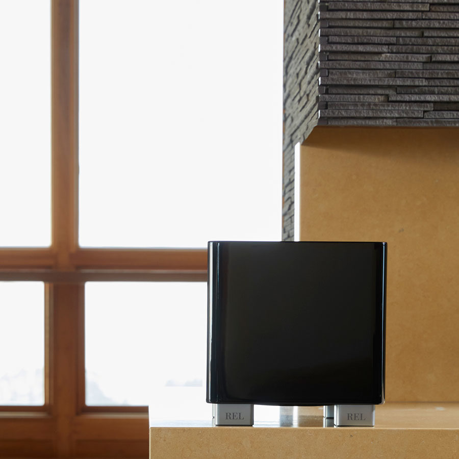 A REL Acoustics T/5x Subwoofer sitting on a counter in front of a window.